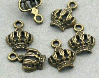 May include: Six antique gold-toned crown charms with a loop for attaching to jewelry or other crafts. The crowns have a detailed design with a pointed top and a decorative base.