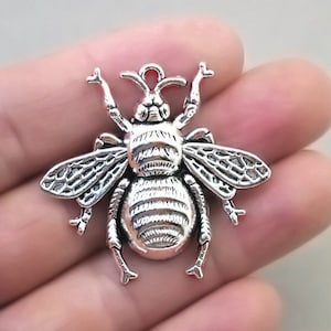 May include: Silver-toned bee charm with detailed wings and a textured body. The charm has a loop at the top for attaching to jewelry or other crafts.