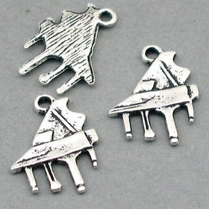 May include: Three silver-toned piano charms with a distressed finish. Each charm features a detailed grand piano design, including the keyboard and legs. The charms have a loop at the top for easy attachment to jewelry or crafts.