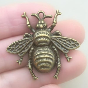 May include: A bronze bee charm with detailed wings and a textured body. The charm has a loop at the top for attaching to jewelry or other crafts.
