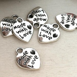 May include: Six silver heart-shaped charms with the text "Made with Love" on each charm. The charms have a loop at the top for attaching to a necklace or bracelet.