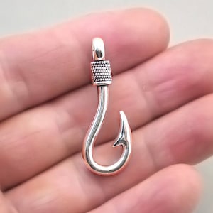 Peut inclure: Breloque en forme d'hameçon de pêche en métal argenté avec un détail texturé en haut. L'hameçon est un motif populaire pour la fabrication de bijoux.