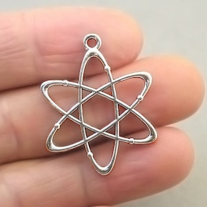 May include: A silver-colored charm in the shape of an atom, featuring a central nucleus with orbiting loops and small bead-like details. The charm has a loop at the top for attaching to a necklace or bracelet. The design is a representation of atomic structure.
