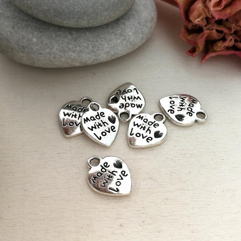 May include: Six silver heart-shaped charms with the text "Made with Love" on each charm. The charms have a loop at the top for attaching to a necklace or bracelet.
