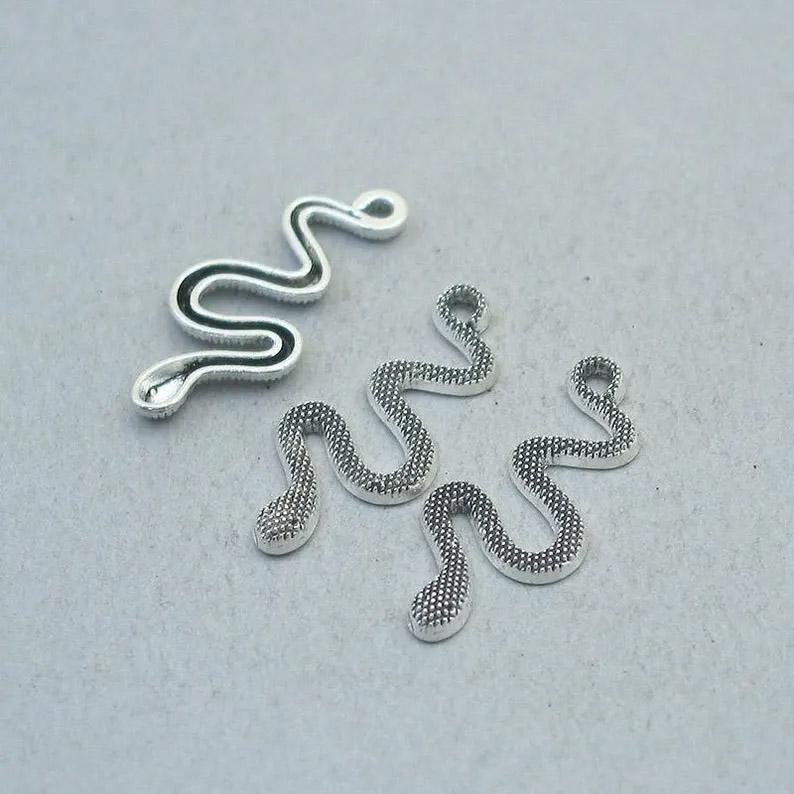May include: Silver-toned snake charms in various sizes. One charm has a black outline, while the others have a textured, dotted pattern. These charms are ideal for jewelry making or crafting projects.