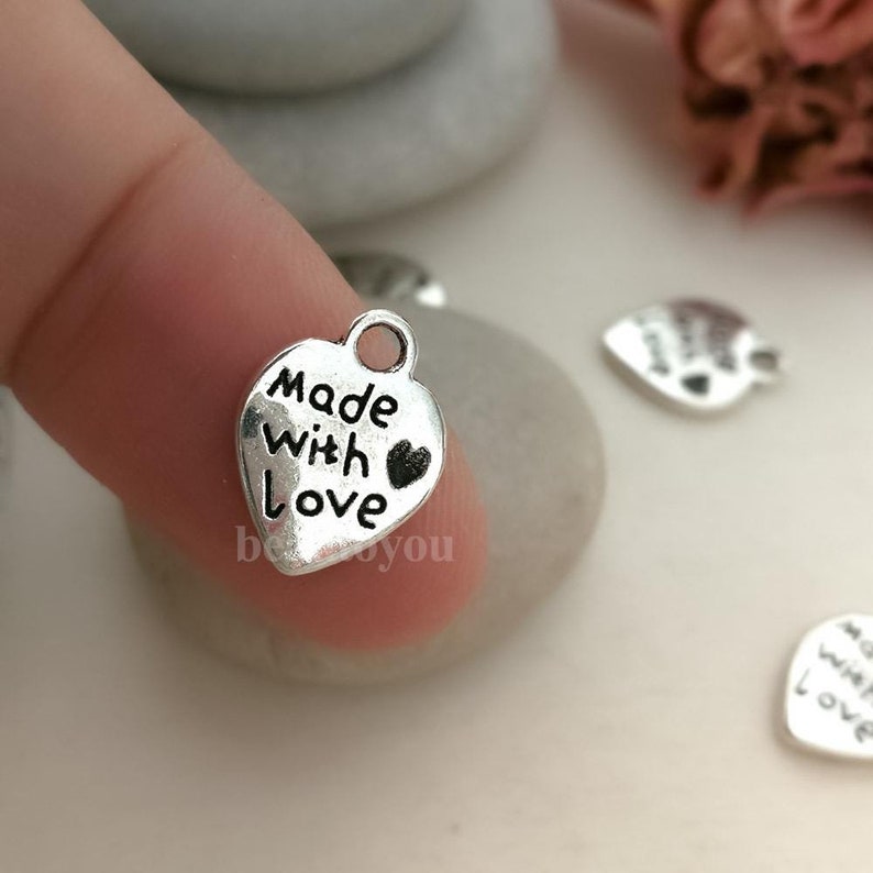 May include: Silver heart-shaped charm with the words "Made with Love" and a small heart symbol.