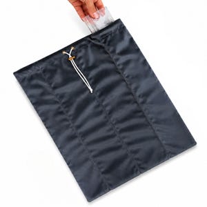 May include: A dark gray rectangular fabric pouch featuring a vertical stitched panel design. The top opening is secured with a white drawstring cord threaded through gold-toned metal eyelets, allowing the bag to be cinched closed for storage.