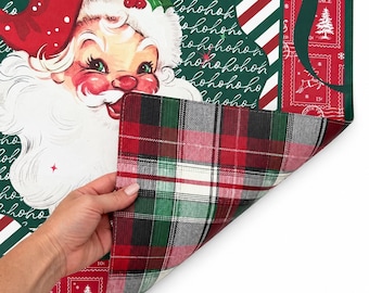 May include: A rectangular placemat featuring a vintage-style Santa Claus illustration on a dark green background with white 'hohoho' text. The reverse side displays a classic red, green, black, and white plaid pattern. Red borders feature postage stamp motifs.
