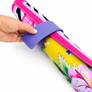 May include: A rolled yoga mat featuring a vibrant floral pattern with yellow, pink, and green hues on one side and a black and white zebra print on the other. The mat is secured with a solid purple silicone strap that wraps around the center.