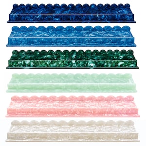May include: A set of six rectangular wall shelves with a scalloped top edge, each featuring a marbled pattern. The shelves are presented in a vertical stack in colors of dark blue, medium blue, dark green, light green, pink, and off-white.