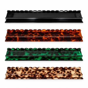 May include: Four rectangular wall shelves with a scalloped top edge. The shelves are made of a smooth, glossy material in four distinct finishes: solid black, dark brown tortoiseshell, translucent emerald green, and light beige tortoiseshell.