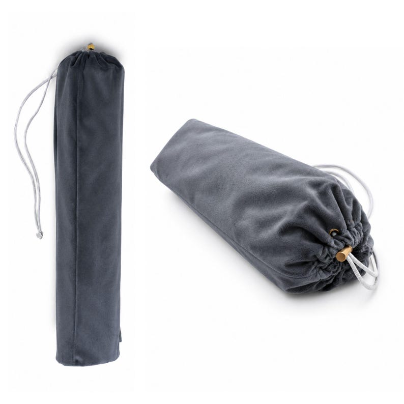 May include: A cylindrical dark gray velvet drawstring bag featuring a soft fabric texture, a white cord closure, and a small metallic gold-toned bead at the end of the drawstring. The bag is shown in both a vertical upright position and a horizontal orientation.