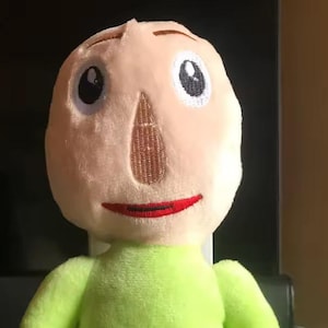 May include: A plush doll of a character with a pale face, large eyes, and a red smile. The doll has a light green body, brown feet, and blue shorts. The arms and feet are a lighter color than the body. The doll is sitting.
