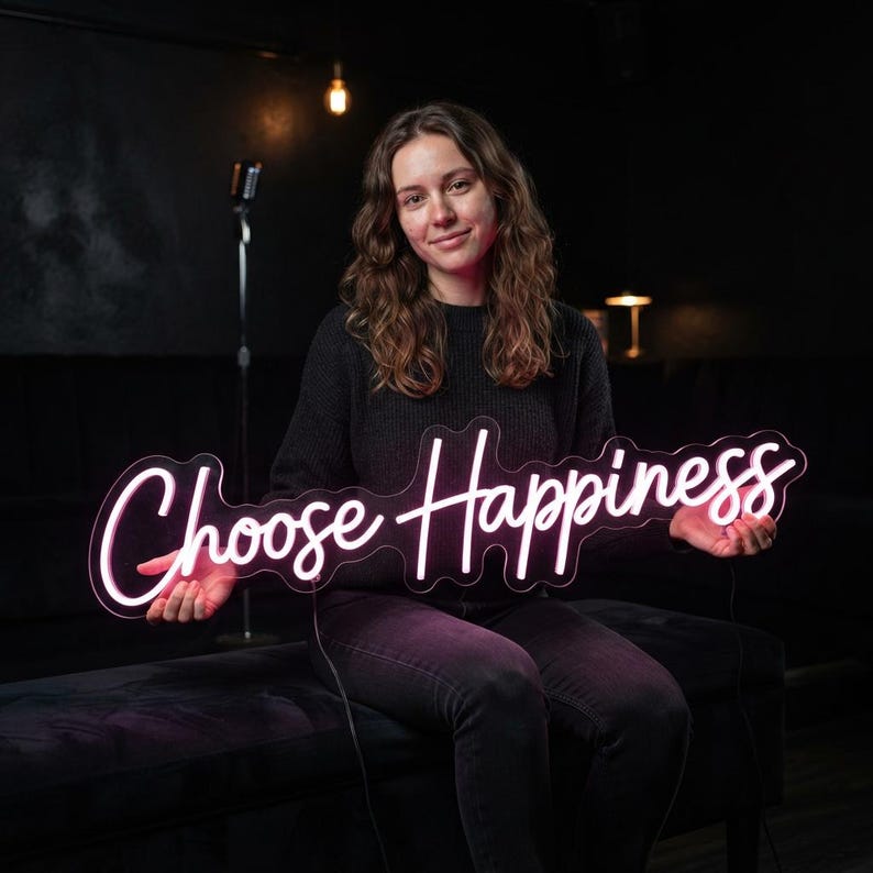 May include: A neon sign featuring the words Choose Happiness in a cursive script font. The sign emits a bright white glow and is mounted on a clear acrylic backing that follows the contour of the lettering. The text is clearly legible and centered.