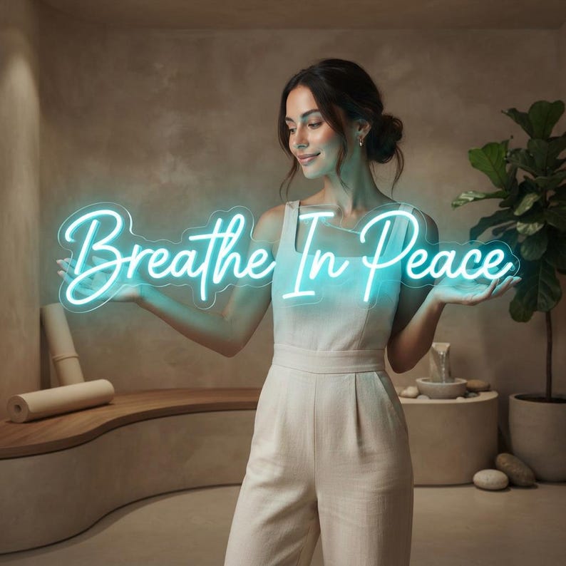 May include: A bright cyan neon sign displaying the text "Breathe In Peace" in a cursive script font. The sign features a clear acrylic backing that follows the contour of the glowing letters, creating a vibrant light display against a neutral background.
