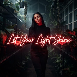 May include: A red neon sign featuring the cursive text Let Your Light Shine. The sign is illuminated with a bright red glow and is held horizontally. The lettering is connected in a flowing script style, creating a vibrant light display.
