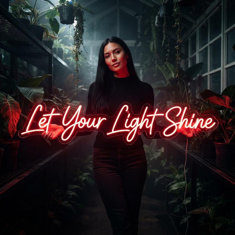 May include: A red neon sign featuring the cursive text Let Your Light Shine. The sign is illuminated with a bright red glow and is held horizontally. The lettering is connected in a flowing script style, creating a vibrant light display.