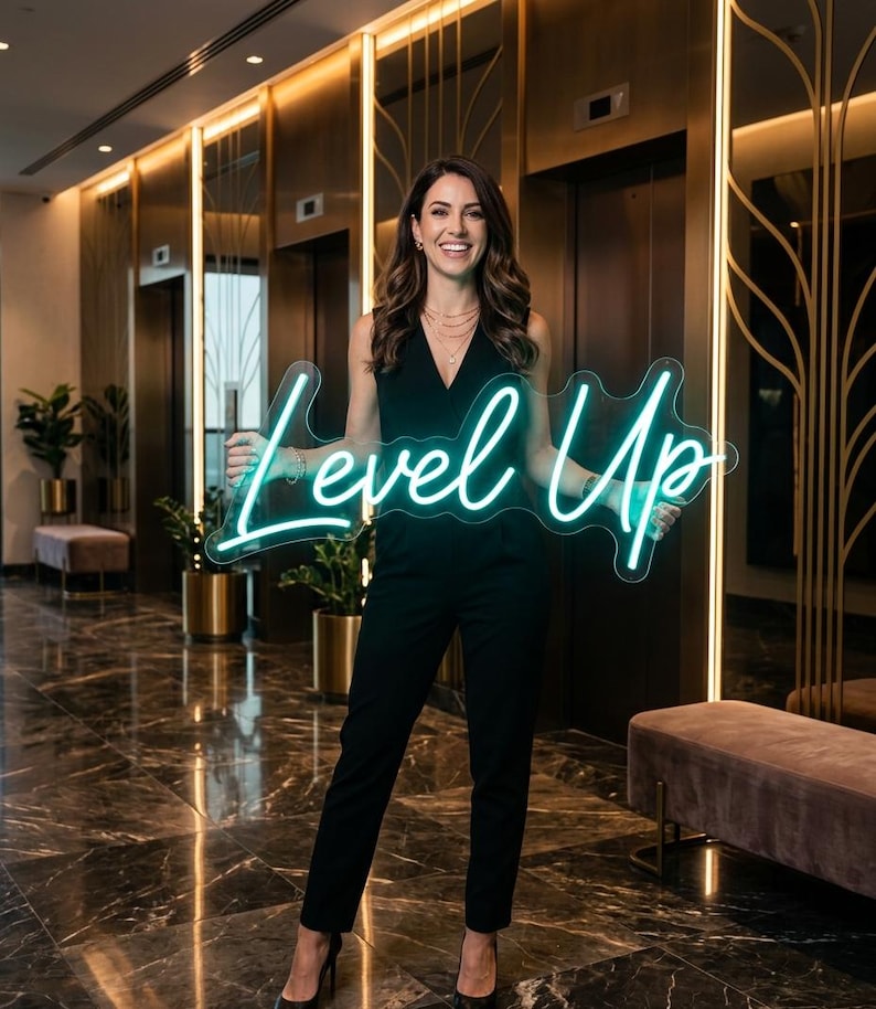 May include: A custom neon sign featuring the words Level Up in a bright teal cursive script. The sign is mounted on a clear acrylic backing cut to the shape of the text. The neon tubing glows with a vibrant light, creating a distinct visual display.