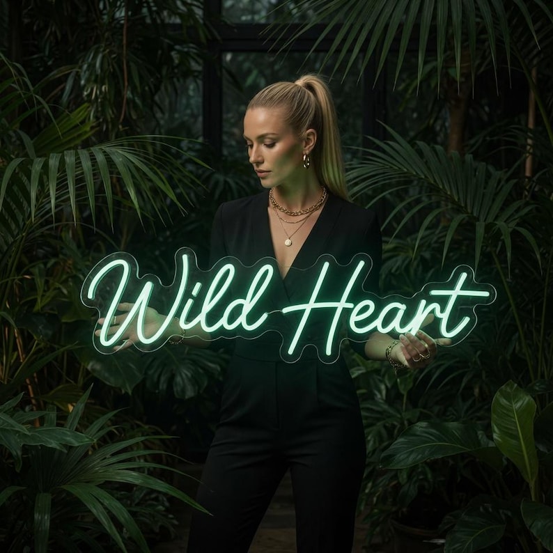 May include: A neon sign featuring the words Wild Heart in a glowing light green cursive script. The sign has a clear acrylic backing cut to the shape of the lettering. The text is illuminated, creating a bright, focused light source.
