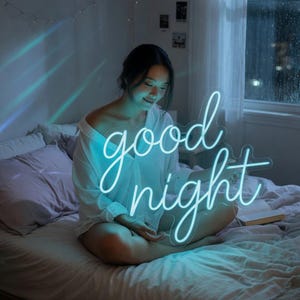 May include: A neon sign featuring the words good night in a cursive script font. The sign emits a bright cyan light, casting a glow on the surroundings. The text is displayed in two lines with the word good above the word night.