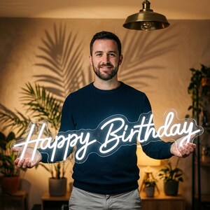 May include: A white neon sign featuring the words Happy Birthday in a cursive script font. The sign is mounted on a clear, contoured acrylic backing and emits a bright, steady glow, displaying the text clearly across the center.