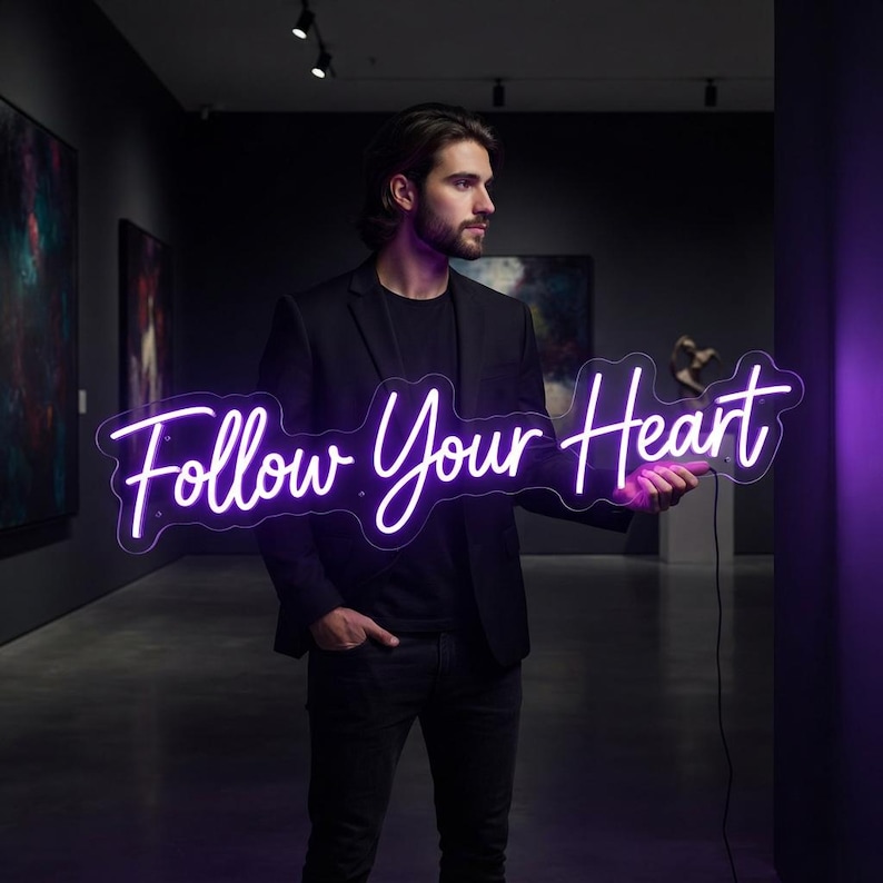 May include: A bright purple neon sign featuring the cursive text Follow Your Heart. The sign is constructed with a clear acrylic backing and is illuminated, casting a vibrant glow. It is held horizontally, displaying the script lettering clearly.