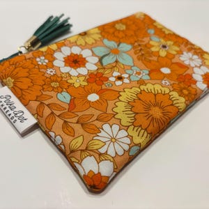 May include: A square, floral patterned pouch in shades of orange, yellow, white, and teal. The pouch has a green tassel and a tag that reads "Polka Dot Threads". The floral design is reminiscent of vintage styles.