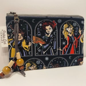 May include: A black zippered pouch with a colorful print of witches and stars. The pouch has a brown leather zipper pull with wooden beads. The text "Polka Dot Threads" is printed on the side of the pouch.