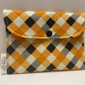 May include: A small, rectangular fabric pouch with a flap closure. The pouch features a repeating pattern of yellow, black, and white checkered squares. A black snap secures the flap. A small tag on the side reads "Polka Dot Threads."