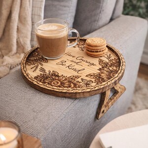 May include: A round wooden sofa arm tray with a floral design and the words "Have Courage and Be Kind" etched into the wood. The tray holds a glass mug of coffee and a stack of cookies.
