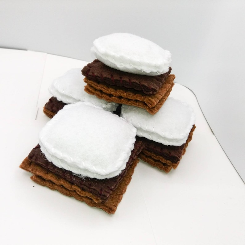 K&ouml;nnte beinhalten: Ein Stapel Filz-S'mores, jede aus zwei braunen Graham-Cracker-Quadraten und einer wei&szlig;en Marshmallow dazwischen.