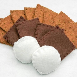 K&ouml;nnte beinhalten: Ein Set aus Filz-Graham-Crackern, Schokoladenquadraten und Marshmallows f&uuml;r ein Spielzeug-S'mores-Bastelprojekt.