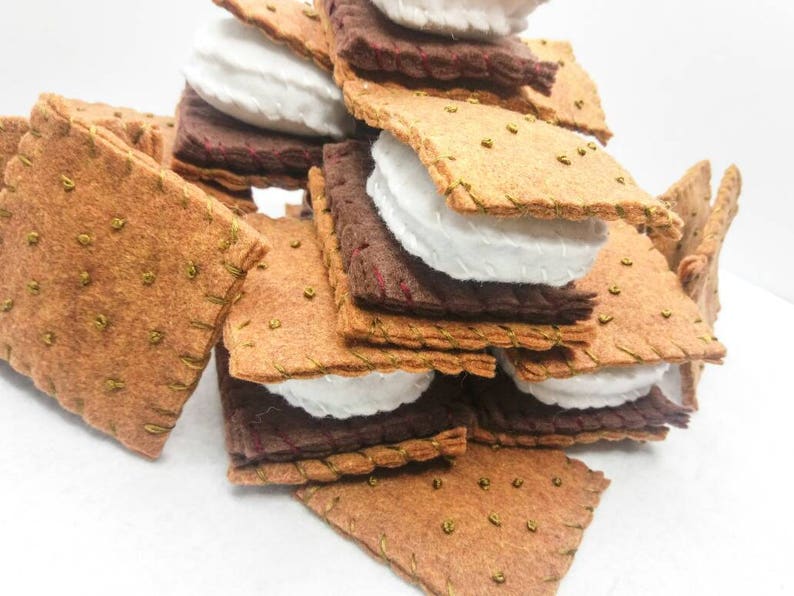 K&ouml;nnte beinhalten: Ein Stapel aus Filz-Graham-Crackern, Marshmallow-Fluff und Schokoladenquadraten, die einem S'more &auml;hneln. Die Filzteile sind zusammengen&auml;ht, um ein realistisches Aussehen zu erzeugen.
