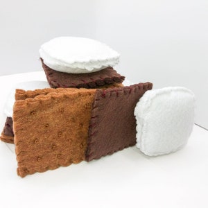 K&ouml;nnte beinhalten: Ein Filz-S'more-Spielzeug mit braunen Graham-Cracker-, braunen Schokoladen- und wei&szlig;en Marshmallow-St&uuml;cken. Die St&uuml;cke sind zusammengen&auml;ht, um ein stapelbares Spielzeug zu schaffen.