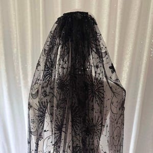 May include: Black veil with a celestial pattern. The sheer fabric is decorated with stars, moons, and sunbursts. The veil is adorned with sequins and is suitable for weddings or special events.
