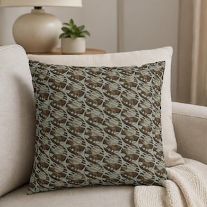 May include: A square throw pillow featuring a repeating pattern of circular motifs. Each circle contains a brown silhouette of an elephant standing against a light blue background with horizontal stripes, creating a consistent graphic design.