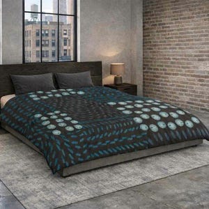 May include: A bed with a dark grey headboard and a patterned duvet cover. The duvet features a repeating design of teal circles and lines on a dark background. The room has a brick wall and large windows.
