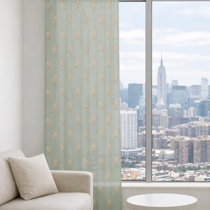 May include: A single floor-length sheer curtain panel in a soft sage green color, featuring a repeating pattern of small, embroidered cream-colored leaf motifs. The curtain is hung from a simple black rod mounted above a large window.