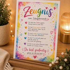 Puede incluir: Una tarjeta rectangular con un borde de acuarela arcoíris y texto en alemán. El encabezado dice Zeugnis zum Schuljahresende, seguido de cinco líneas de texto con iconos de corazones de colores. El texto inferior dice Du bist großartig.
