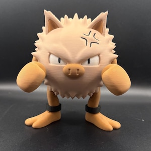 May include: A light tan, spiky-haired figurine with a round body, two large fists, and two feet. The figure has a pig-like snout, narrow eyes, and a black angry vein symbol on its forehead. It wears two black rings around its ankles.