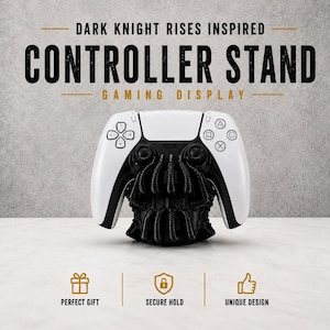 May include: A white and black controller stand with the text "DARK KNIGHT RISES INSPIRED CONTROLLER STAND GAMING DISPLAY". The stand has a unique design and is a perfect gift.