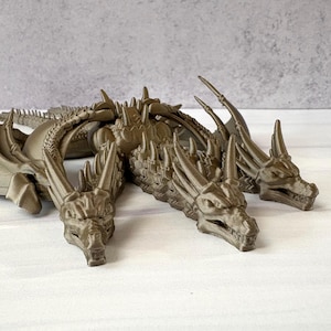 May include: A detailed, three-headed dragon figurine in a metallic bronze color. The dragon has intricate scales, sharp spines, and large wings. The sculpture is posed lying down, with its heads facing forward.