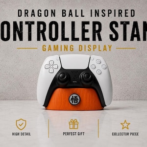 May include: A white and black gaming controller resting on an orange controller stand. The stand has a Japanese symbol on the front. Text at the top reads "DRAGON BALL INSPIRED CONTROLLER STAND GAMING DISPLAY."