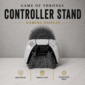 May include: A white and black gaming controller stand with the text "Game of Thrones Controller Stand Gaming Display." The stand is designed to resemble the Iron Throne, with a controller resting on it. The stand is a collector's piece.