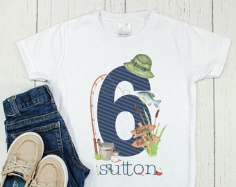 Puede incluir: Camiseta blanca con un número seis azul, una caña de pescar, un cubo y un cartel que dice "Gone Fishing". La camiseta también tiene el nombre "sutton" impreso en ella.