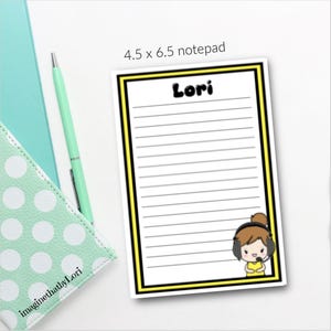 May include: A lined notepad with a yellow and black border, featuring the name "Lori" at the top. A cartoon character with a headset is in the lower right corner. The notepad measures 4.5 x 6.5 inches.