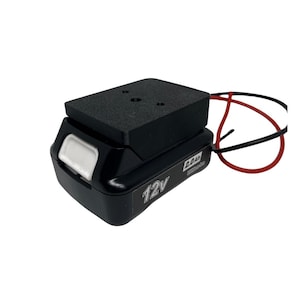 Pode incluir: Uma bateria preta de iões de lítio de 12V com uma capacidade de 2,0Ah. A bateria tem um botão branco e uma parte superior preta. Fios vermelhos e pretos estendem-se da parte superior. O texto "12V" é visível na lateral.