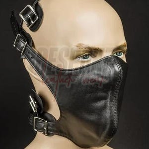 Puede incluir: M&aacute;scara facial de cuero negro con correas ajustables y hebillas met&aacute;licas. La m&aacute;scara cubre la nariz y la boca, con un dise&ntilde;o cosido en la parte delantera. Tiene una correa sobre la cabeza y alrededor del cuello.