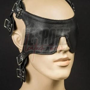 Puede incluir: Antifaz de cuero negro con correas y hebillas ajustables. El antifaz cubre los ojos y tiene una correa que rodea la cabeza. El texto "BESPOKE Leather" es visible en el antifaz.