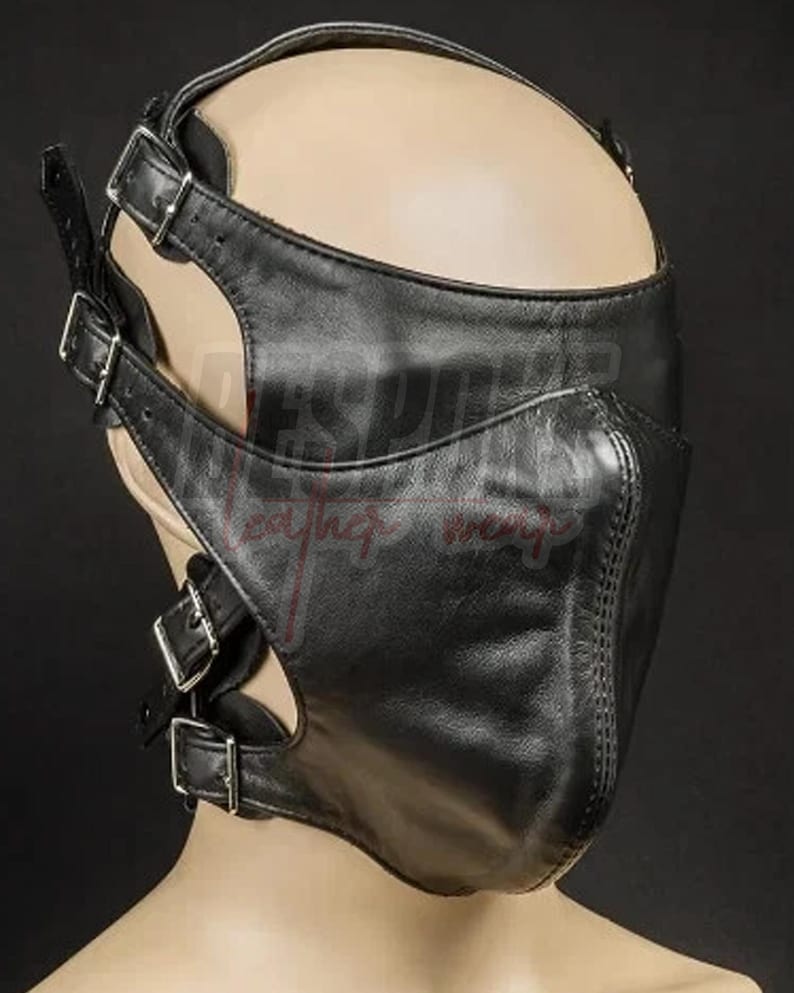 Puede incluir: M&aacute;scara facial de cuero negro con m&uacute;ltiples correas y hebillas plateadas. La m&aacute;scara cubre la nariz y la boca, con cortes alrededor de los ojos y las mejillas. La m&aacute;scara est&aacute; dise&ntilde;ada con una forma contorneada y costuras.